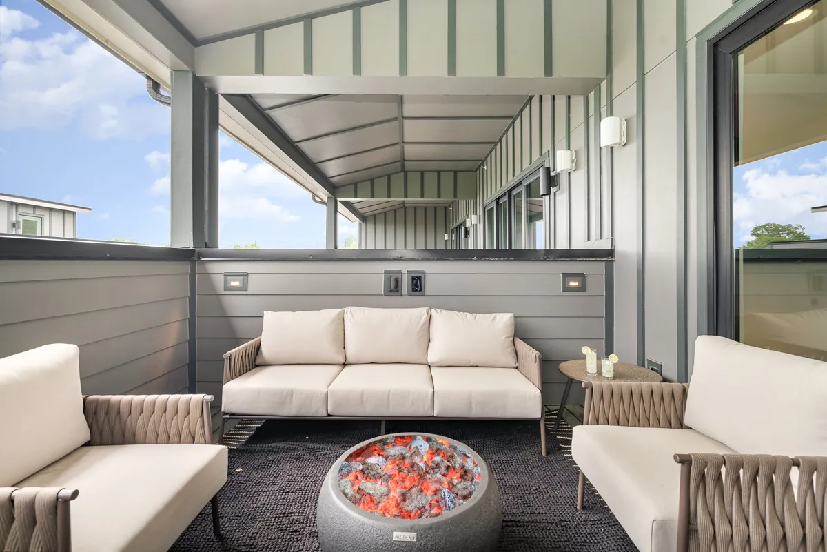 An inviting rooftop seating area with a plush sofa surrounding a modern fire pit. The space is enclosed by stylish walls, offering privacy while still providing an open view of the outdoors—ideal for cozy gatherings and evening relaxation.