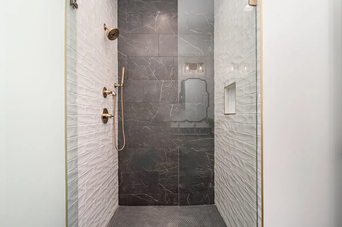 A luxurious walk-in shower with a rain shower head, striking black marble and white textured tiles, and gold fixtures, creating a spa-like setting that invites relaxation after a long day.