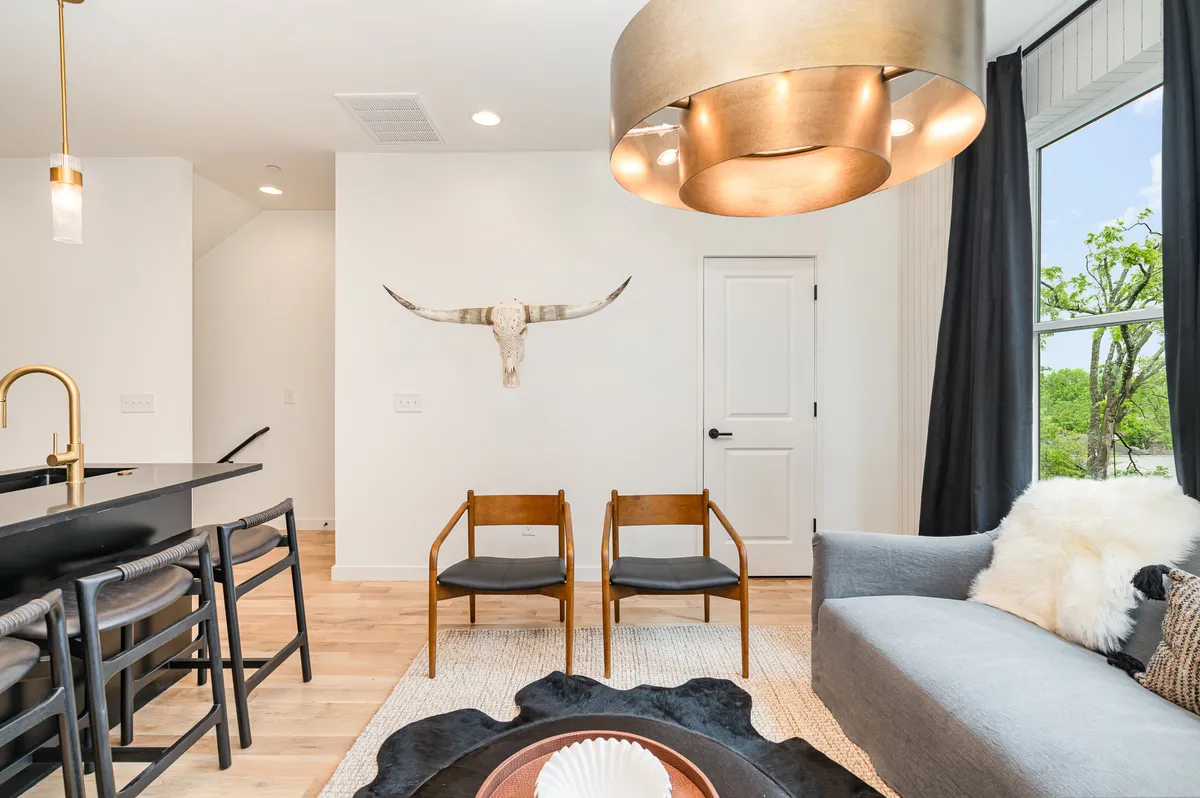 A lounge area featuring a sofa, black chairs, a modern light fixture, and unique wall decor including a cow skull. The arrangement is designed for conversation and relaxation, with a blend of inviting warmth and edgy, contemporary style.