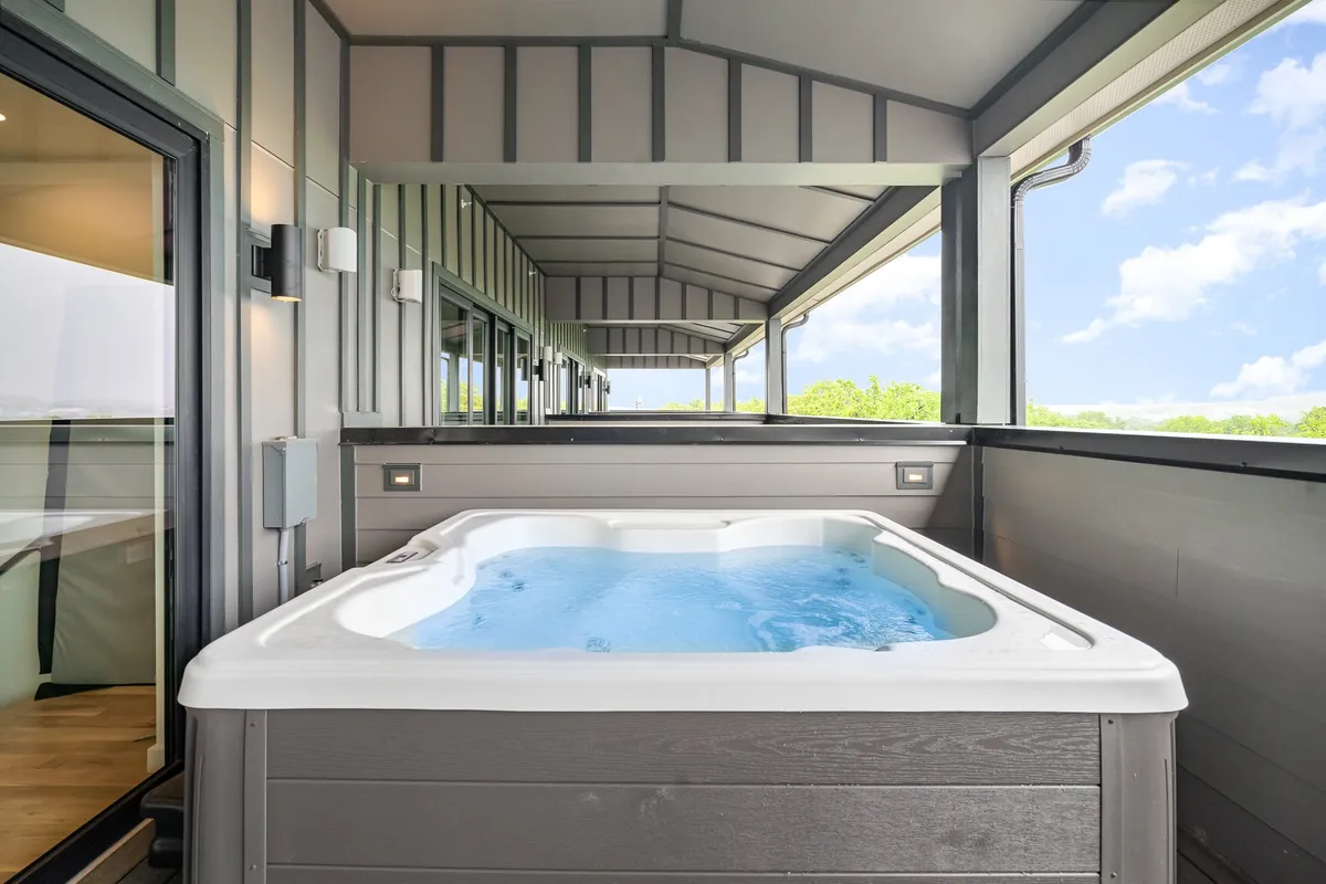 A modern rooftop deck with a hot tub, expansive deck space, and open sky. The view includes the surrounding cityscape, suggesting a prime vantage point for enjoying the Nashville skyline, whether by day or night.