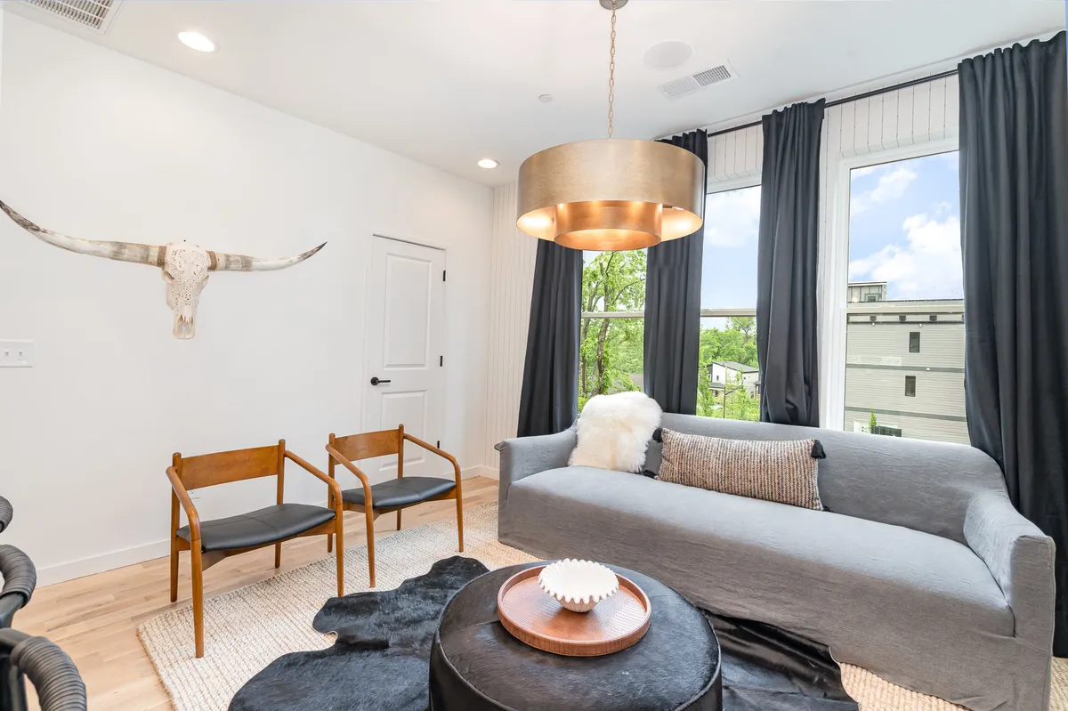 A stylish living room featuring a comfortable sofa, a statement chandelier, a cowhide rug, and modern decorative accents such as a decorative bowl and horn decor. Large windows provide natural light and a view, creating a cozy yet chic ambiance. The arrangement encourages both group gatherings and relaxed solo moments.