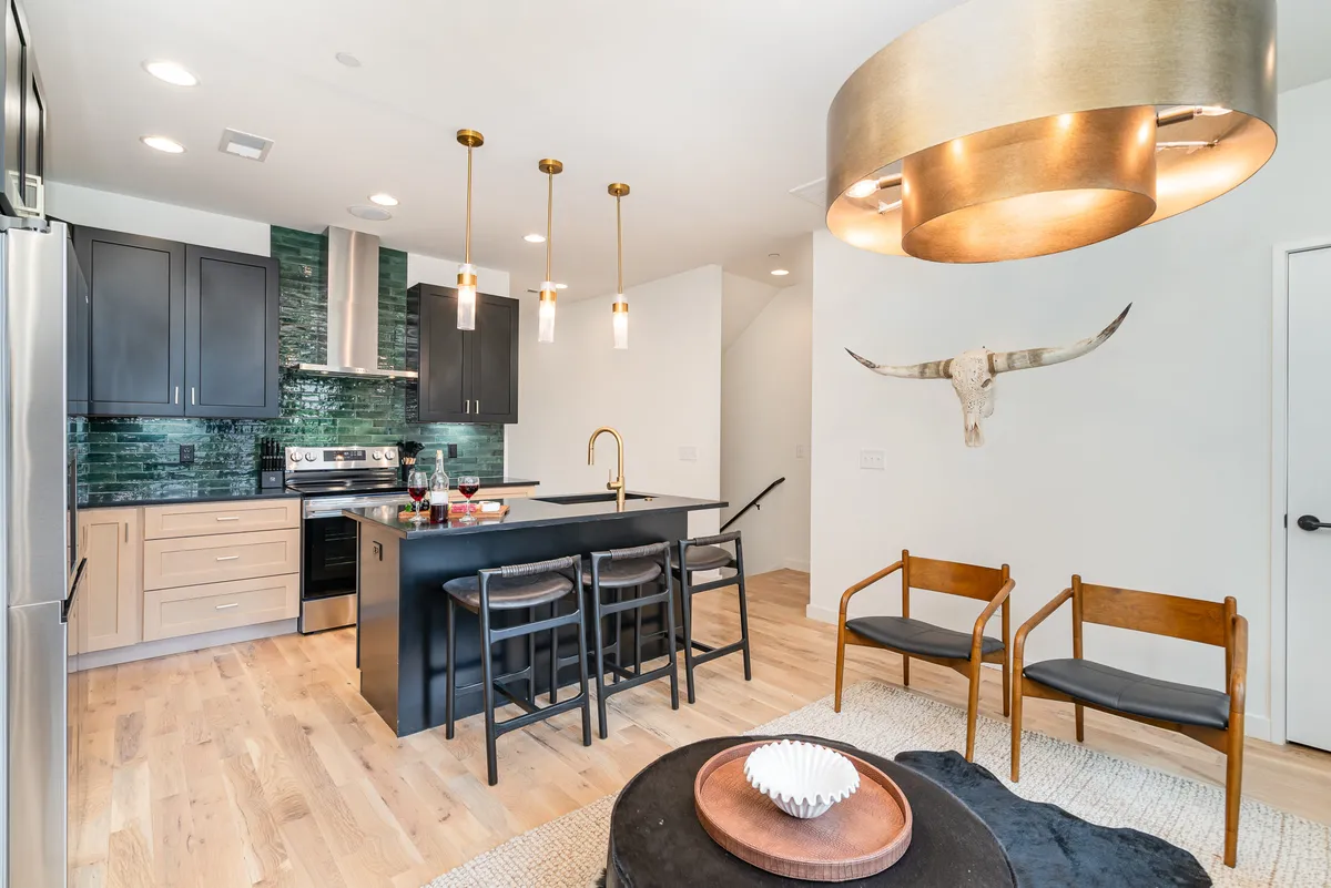 A contemporary kitchen scene with a central island, pendant lighting, a vibrant green backsplash, and distinctive bull skull décor. Wooden chairs at the island offer casual dining or conversation space, and the area radiates a friendly, welcoming vibe.